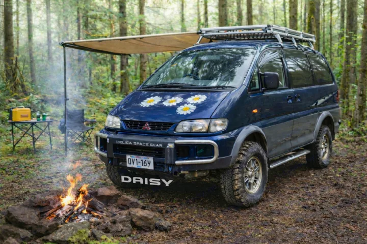 Adventure-ready Mitsubishi Delica campervan, named Daisy, set up in a lush forest with a campfire. Perfect for an rv rental outdoor escape!. MITSUBISHI Delica 1997