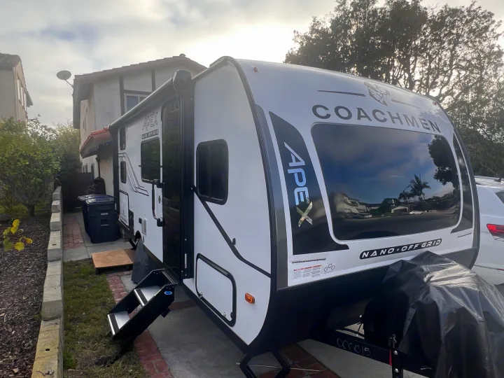 Coachmen Apex Nano Off Grid RV rental, a white travel trailer parked in a residential setting with steps extended.. Coachmen Apex Nano 194BHS 2026