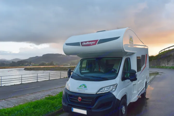 A white Challenger **rv rental** is parked by an estuary and hills under a dramatic cloudy sunset sky.. CHALLENGER C194 START EDITION 2026
