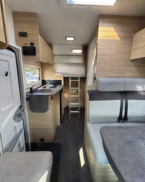 RV rental interior: well-lit space with a kitchenette, dining area featuring gray seats, and an overhead bunk bed with a ladder.. CHALLENGER C194 START EDITION 2026