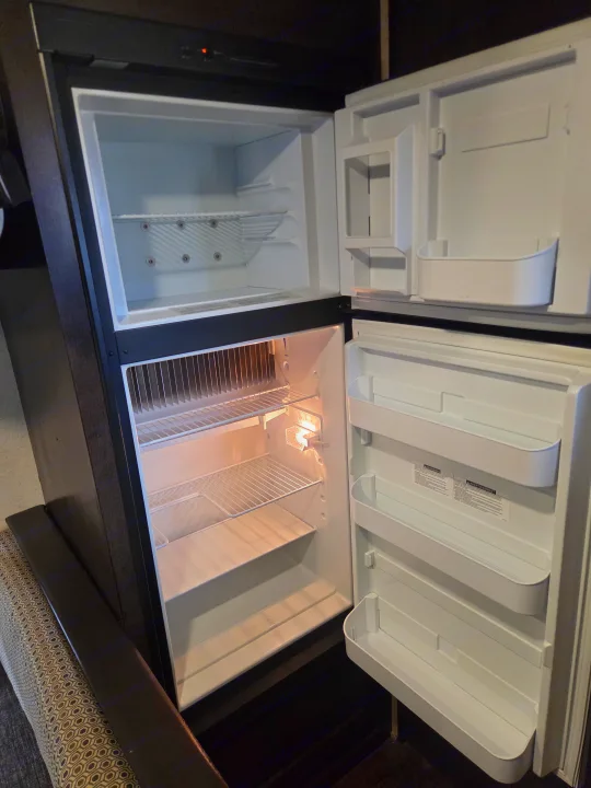 An RV rental's open refrigerator and freezer, both empty, with bright interior lights and shelves, ready for your journey.. Forest River Salem Cruise Lite 2018