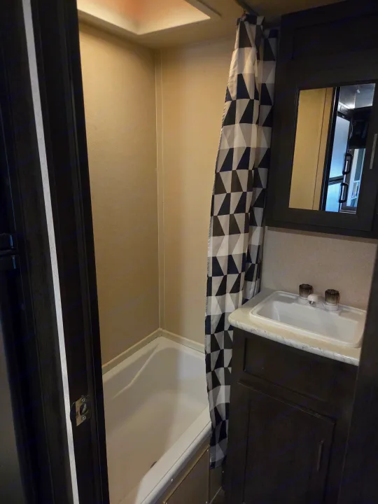 Compact RV rental bathroom with tub/shower, geometric curtain, and dark wood vanity with sink and mirror.. Forest River Salem Cruise Lite 2018