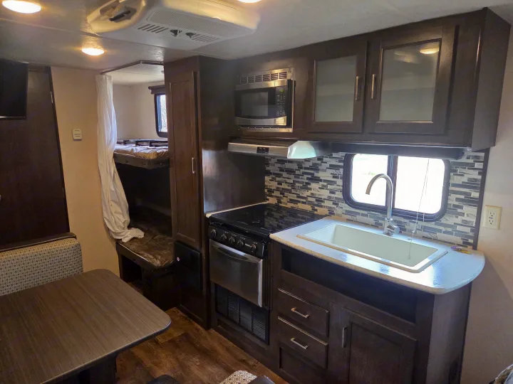 Spacious RV rental interior featuring a full kitchen with microwave, sink, and stove, a cozy dinette, and bunk beds.. Forest River Salem Cruise Lite 2018