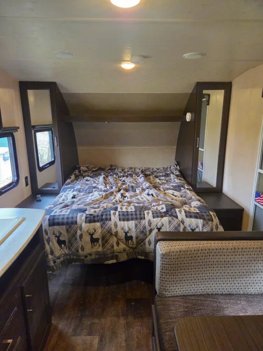 Inside this rv rental, a cozy bedroom with a deer-patterned bed, built-in storage, and dinette seating is visible.. Forest River Salem Cruise Lite 2018