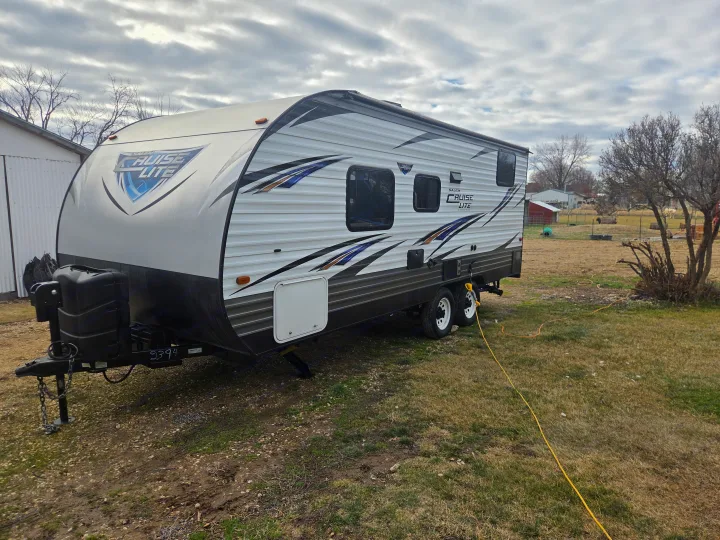 This Salem Cruise Lite travel trailer RV rental is set up outdoors on grass, hooked up with a yellow power cord, under cloudy skies.. Forest River Salem Cruise Lite 2018