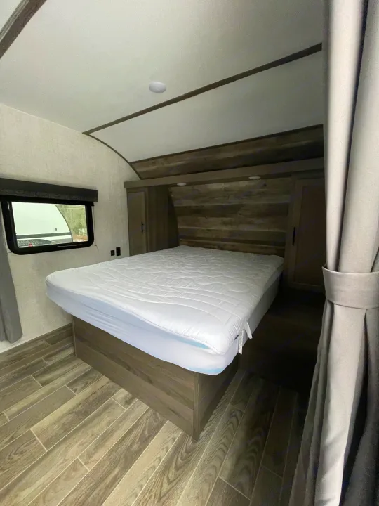 Cozy rv rental bedroom interior with a white bed, window, and stylish wood-look floor. Ready for your adventure.. Gulf Stream Friendship 2022