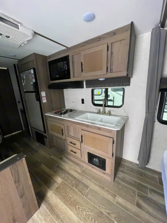 Clean RV rental kitchen featuring microwave, stovetop, dual sink, and modern wood-look flooring and cabinets.. Gulf Stream Friendship 2022