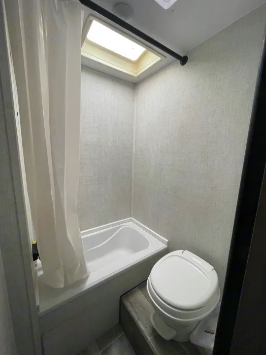 Essential RV rental bathroom setup: compact tub/shower, toilet, and a natural light skylight for comfort.. Gulf Stream Friendship 2022