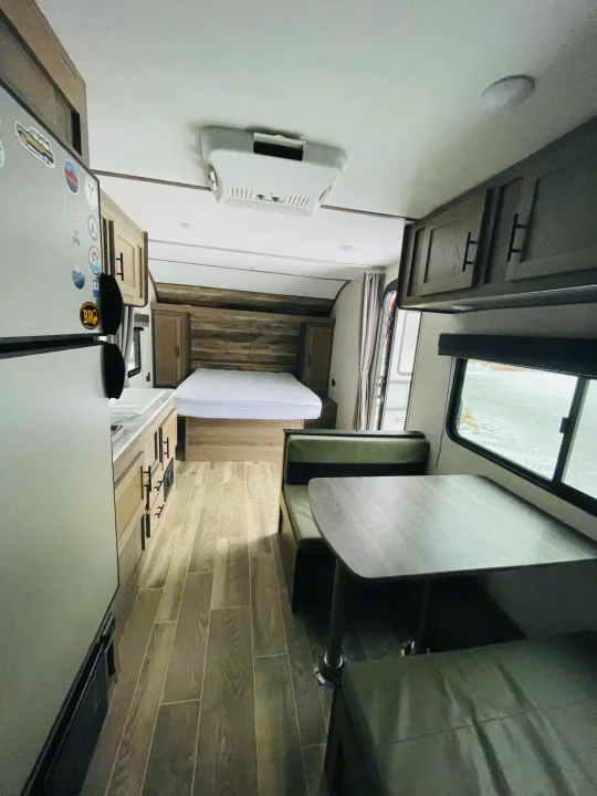 Interior of an rv rental with a bed, kitchenette (fridge, sink), and dinette with benches. Features wood-look flooring.. Gulf Stream Friendship 2022