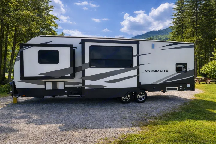 This white and gray Vapor Lite RV rental is set up at a scenic campsite, perfect for outdoor trips.. Keystone RV Fuzion Toy Hauler 2020