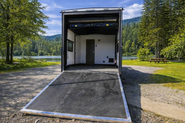 This RV rental toy hauler, with its ramp open, is perfectly parked by a beautiful lake and forest, ideal for adventure.. Keystone RV Fuzion Toy Hauler 2020