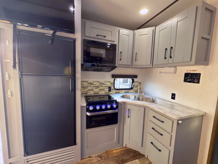 Modern RV rental kitchen featuring a refrigerator, microwave, stove, and sink. Ideal for travel trailer adventures.. Keystone RV Fuzion Toy Hauler 2020