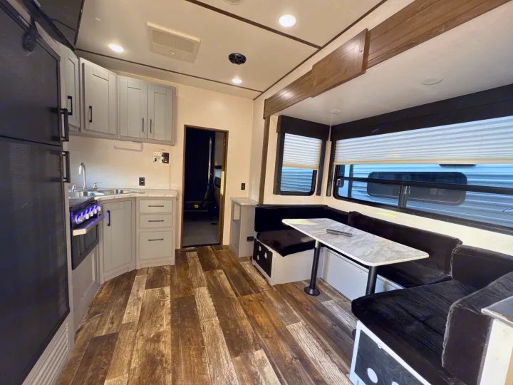 Bright rv rental interior showing a light gray kitchen, oven with blue lights, dark dinette, and wood-look floor.. Keystone RV Fuzion Toy Hauler 2020