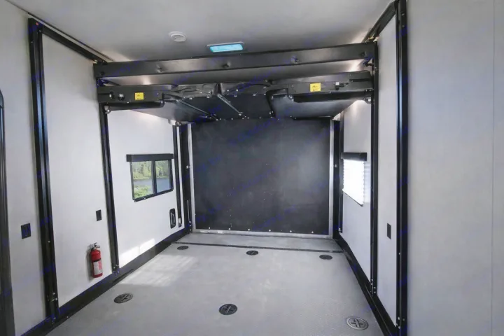 Spacious RV rental cargo area with grey, textured floor, tie-downs, windows, fire extinguisher, and an overhead retractable bed.. Keystone RV Fuzion Toy Hauler 2020