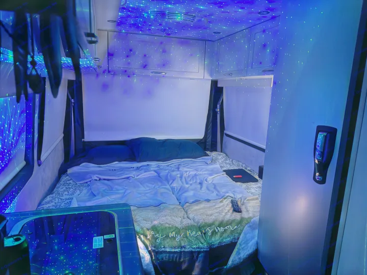 Dreamy rv rental bedroom with a galaxy of blue and green lights on the ceiling, a comfortable bed, and compact storage in this camper.. Pleasure-Way Pleasure-Way Class B 2020