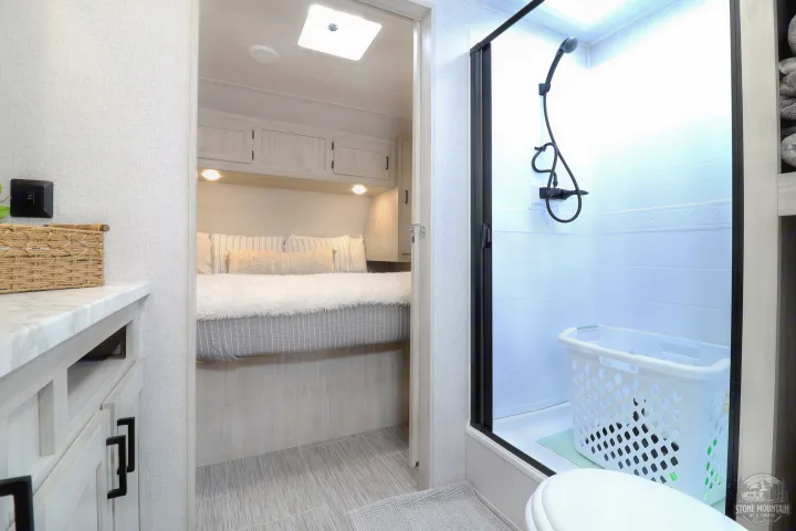 Clean rv rental interior showing a cozy bedroom with overhead cabinets, and a modern bathroom with a shower and toilet.. East to West Silver Lake 2023