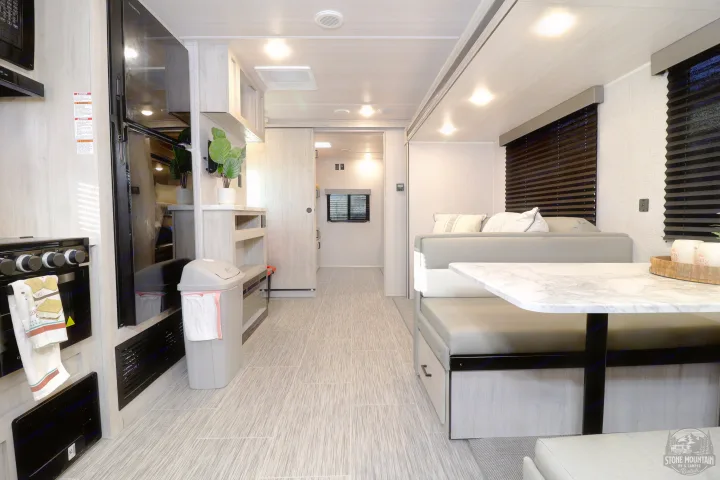 Modern rv rental interior showcasing a full kitchen, dining area, and hallway with light wood cabinetry and gray-patterned flooring.. East to West Silver Lake 2023