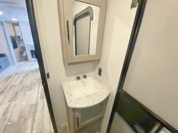 Compact RV rental bathroom with vanity & sink, offering a peek into the cozy living area with wood floors.. Coleman Lantern 2021