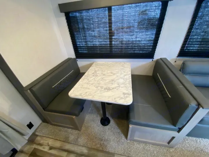 RV rental dinette: cozy gray booth seating with wood bases & marble table, ideal for meals & relaxation.. Coleman Lantern 2021