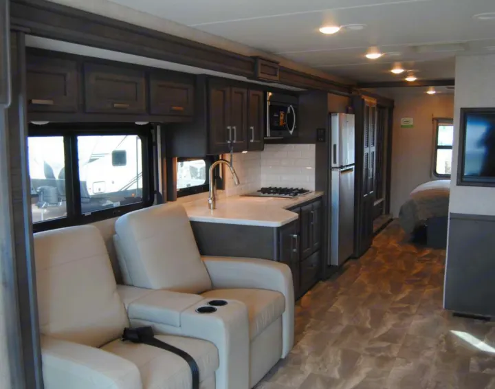 Modern RV rental interior with comfortable recliners, a full kitchen, and a glimpse of the bedroom. Ready for travel!. Thor Challenger 2023