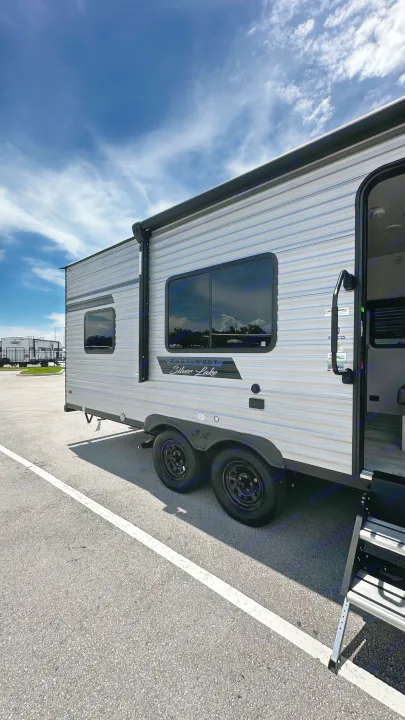 Silver Lake RV rental: A sleek travel trailer, with dual axles & entrance steps, parked on asphalt under a sunny sky.. East to West Silver Lake 2024