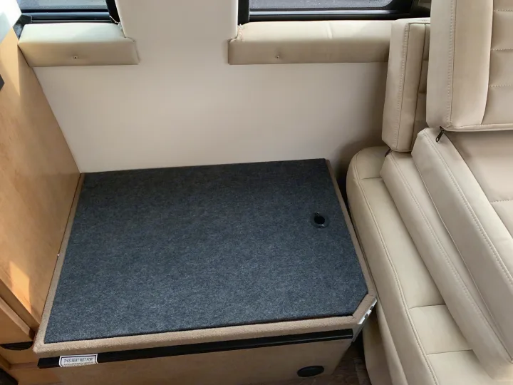 RV rental interior showcasing cream seating and a multi-purpose storage box/seat with a warning label. Perfect for travel setups.. Coachmen Galleria 2020