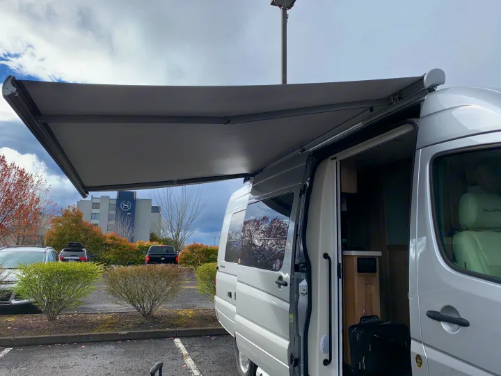This RV rental with an extended awning and open door shows a suitcase, parked near a Sheraton hotel.. Coachmen Galleria 2020