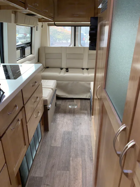 Interior of an RV rental showcasing a modern kitchenette, light seating, and wood-look flooring down the aisle.. Coachmen Galleria 2020