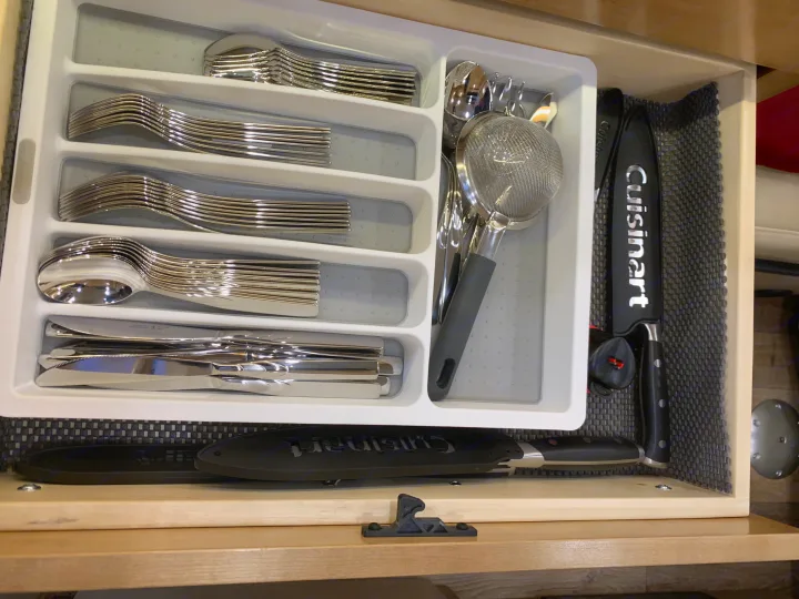 Organized cutlery, a strainer, and Cuisinart knives neatly arranged in an RV rental kitchen drawer with a non-slip mat.. Coachmen Galleria 2020