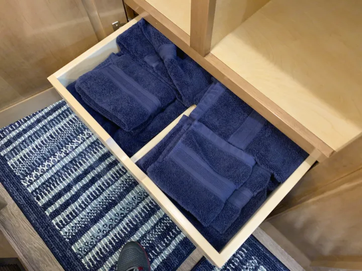 Clean navy towels neatly folded in an RV rental drawer, with a blue patterned rug on the floor and light wood cabinetry.. Coachmen Galleria 2020