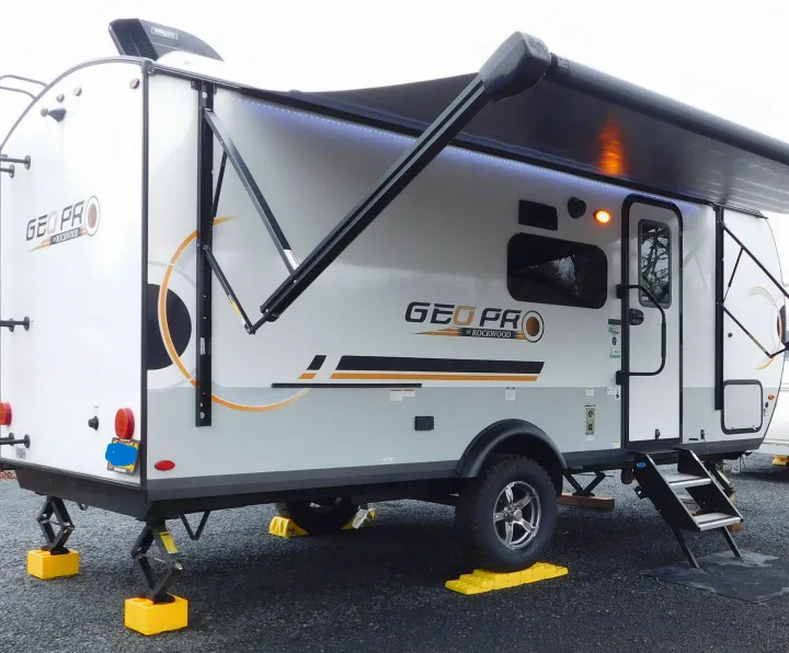 Modern Geo Pro by Rockwood travel trailer, an ideal RV rental, showcasing an extended awning, lights, and leveling for camping.. Forest River GeoPro 20BHS 2022