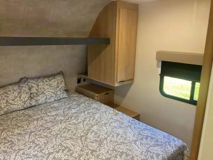 RV rental: Cozy bedroom with patterned bedding, an overhead shelf, wood cabinets, and a window.. Winnebago Minnie Winnie 2024