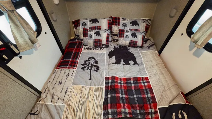 Cozy RV rental bed with rustic bear, tree, and plaid bedding. Ready for adventure and restful nights on the road!. Forest River Rockwood Geo Pro 2018