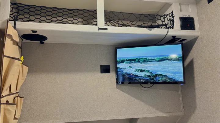 RV rental interior with JVC TV, Furrion panel, overhead bunk with net storage, and a fabric wall organizer.. Forest River Rockwood Geo Pro 2018