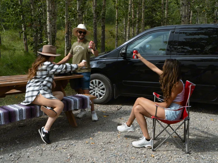 Three friends enjoy drinks by their vehicle in nature, a perfect stop on an RV rental journey.. Glacier Campers Cosy CrewVan 2015