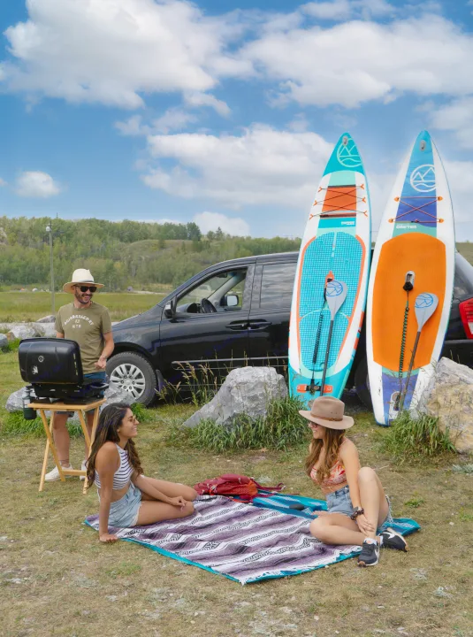 Friends gather by their rv rental, grilling and paddleboarding, enjoying a sunny day outdoors.. Glacier Campers Cosy CrewVan 2015