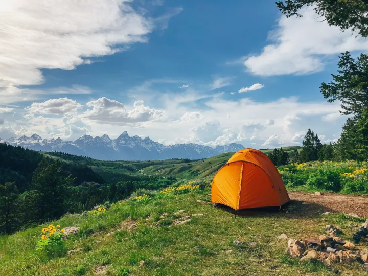 Experience serene nature: an orange tent on a grassy hill overlooking majestic mountains. Imagine this view from your RV rental.. Glacier Campers Cosy CrewVan 2015