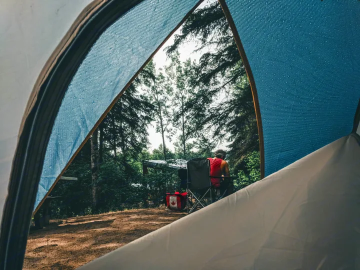 Cozy tent view looking out at a person relaxing at a forested campsite, ideal for an RV rental adventure. Raindrops on tent.. Glacier Campers Cosy CrewVan 2015