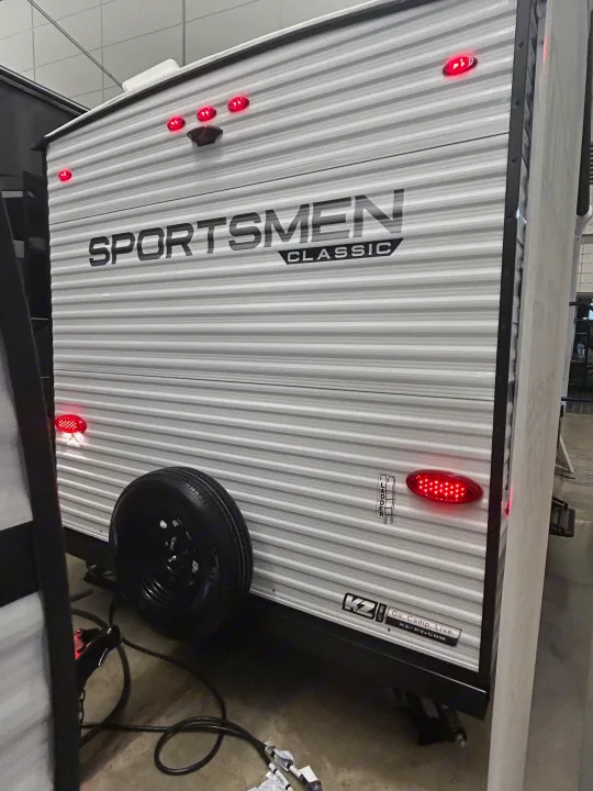 Rear view of a KZ Sportsmen Classic travel trailer, featuring red lights, backup camera, and a spare tire. Ideal for an RV rental adventure.. K-Z 130RD 2026