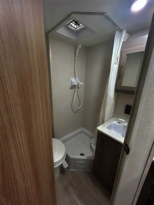 Modern RV rental bathroom: compact corner shower, toilet, and vanity with sink. Clean, light grey interior design.. K-Z 130RD 2026