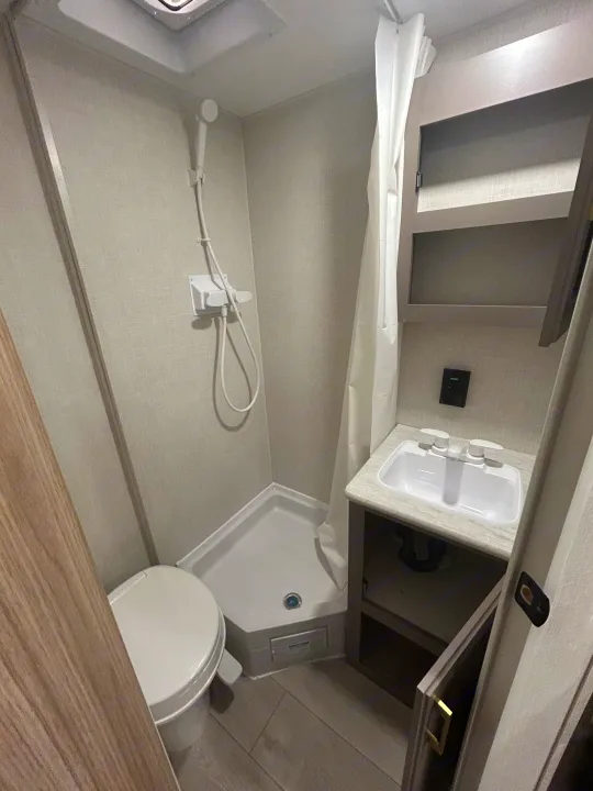 Inside an RV rental, this compact bathroom features a white toilet, shower, and sink with light-colored walls.. K-Z 130RD 2026