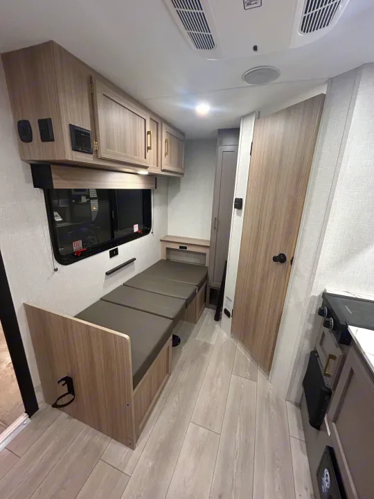 RV rental interior featuring a convertible dinette/bed, modern light wood cabinetry, compact kitchen, and storage.. K-Z 130RD 2026