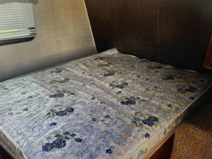 RV rental bedroom: Cozy interior with a patterned mattress, window with blinds, and textured walls, ready for your travels.. Springdale Sumerland mini 2015