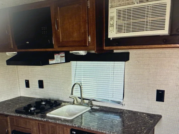 RV rental interior: A compact kitchen with sink, gas stovetop, microwave, overhead cabinets, and AC unit.. Springdale Sumerland mini 2015