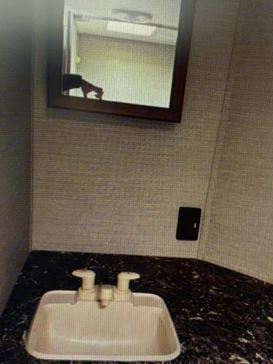 RV rental bathroom interior with a white sink, dark counter, and mirror reflecting a hand and overhead light. Practical design.. Springdale Sumerland mini 2015