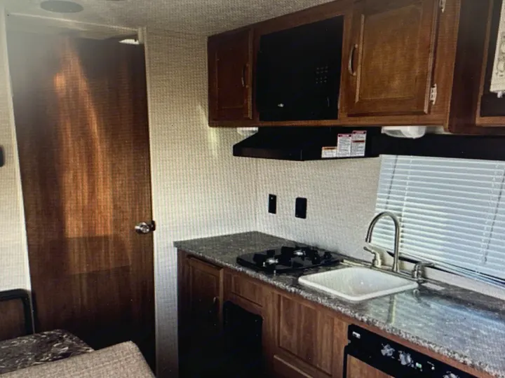 RV rental kitchen: interior with stove, sink, microwave, wood cabinets & door. Ready for travel cooking.. Springdale Sumerland mini 2015