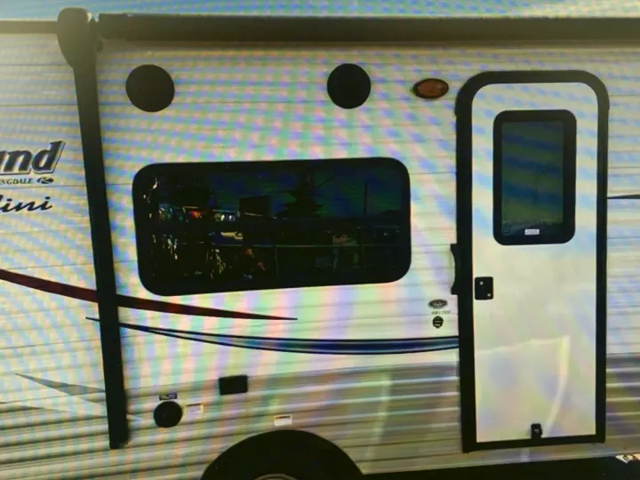 Side of an rv rental, a white travel trailer with a door, window showing reflections, and an awning arm.. Springdale Sumerland mini 2015