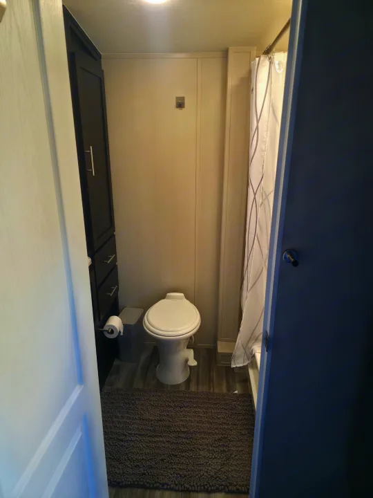 RV rental bathroom with compact toilet, shower, tall cabinet, gray bath mat, and wood-look floor.. Dune Sport Dynamite 2023