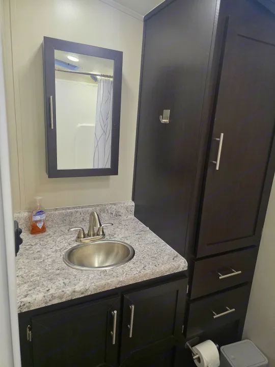 Compact RV rental bathroom with dark vanity, speckled countertop, sink, modern faucet, and mirrored medicine cabinet for storage.. Dune Sport Dynamite 2023