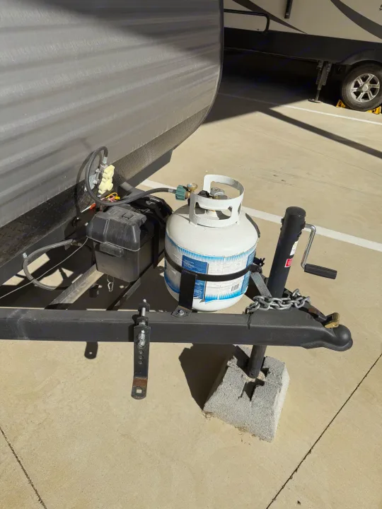 This RV rental's front hitch area features a propane tank, battery, and trailer jack on concrete.. Keystone RV Coleman Lantern 2025